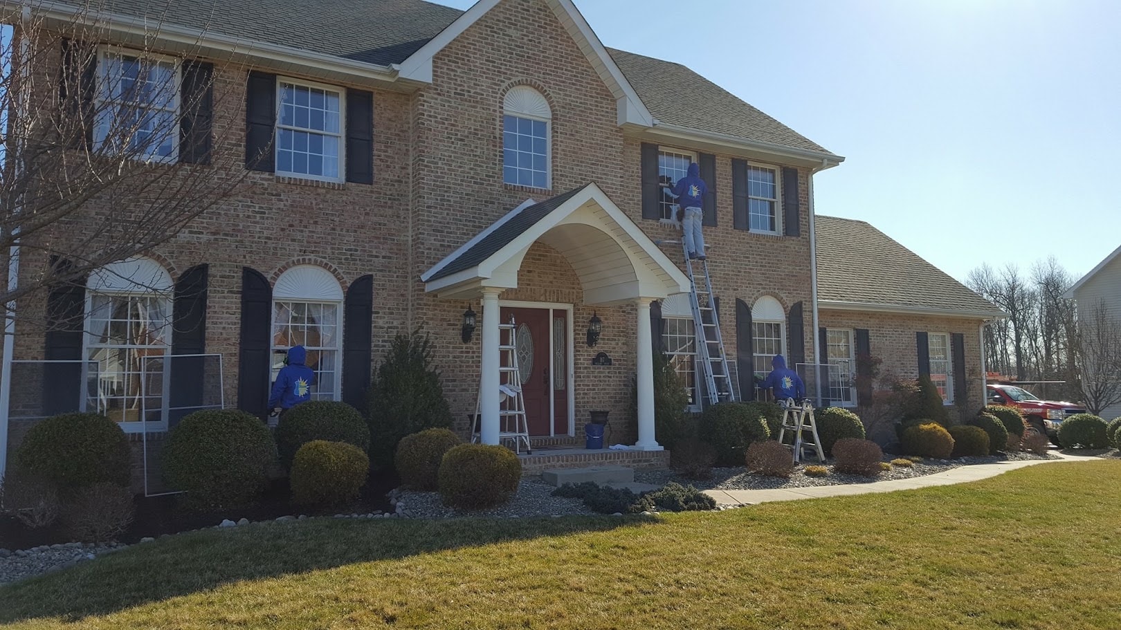 Three professional window cleaners working on a brick home exterior